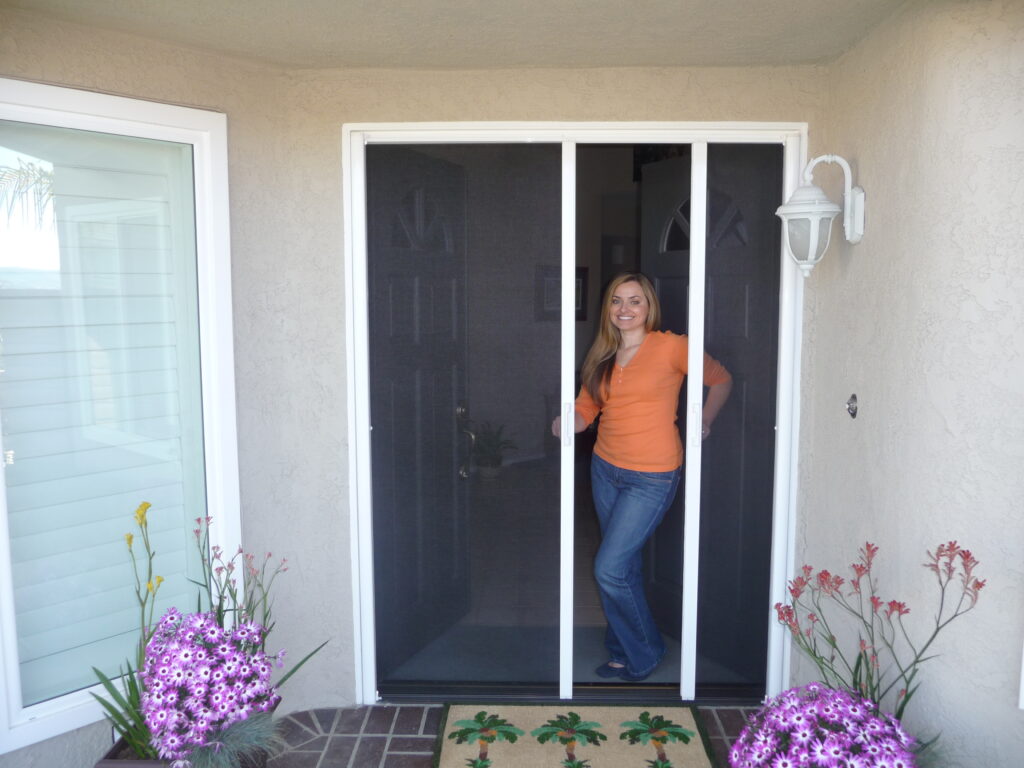 Woman in doorway with retractable screen. Flowers nearby.